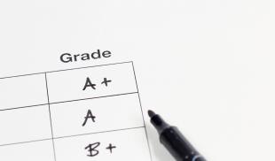 A freshly graded report card—featuring an A +, A and B + grades—with a felt-tip pen laying beside it.
