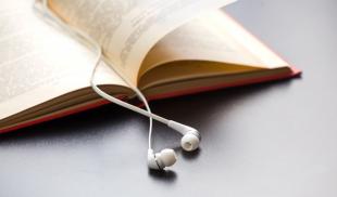 A book lies open on a desk, with a pair of white ear-buds acting as a bookmark.