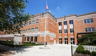 An exterior shot of a school with a flag pole in the courtyard on a sunny day.