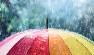 Rain falls on a rainbow-colored umbrella.