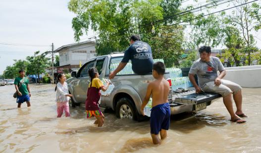 A group of people wading through a flooded street to a pick-up truck to receive containers of water.