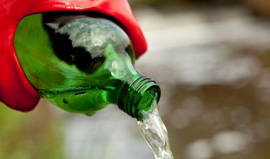An environmental researcher wearing red rubber gloves pours water out of a green bottle.
