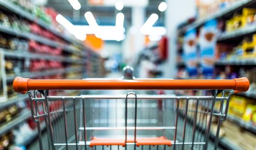 View of an empty shopping cart as seen from the perspective of the shopper, with the aisle blurred.