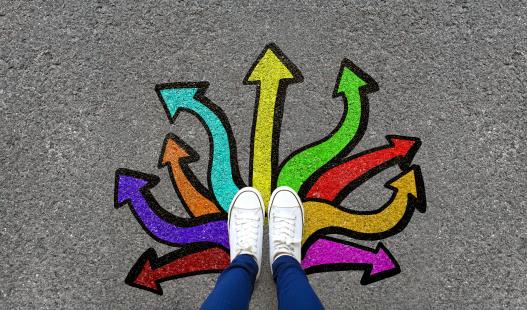 Birds eye view of a pair of shoes on cement, with multicolored arrows pointing from the shoes in different directions.