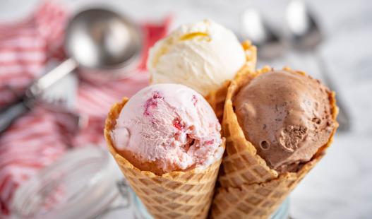 chocolate, strawberry, and vanilla ice cream scoops in cones, with an ice cream scooper in the background