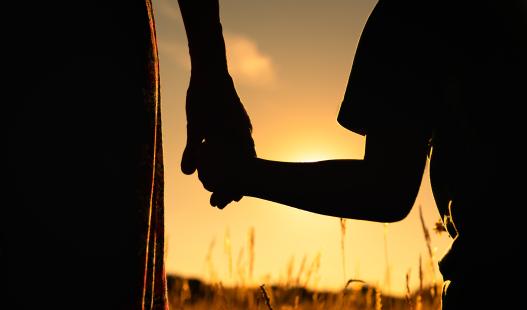 Silhouette of mother and child holding hands facing the sunset.