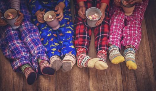 Four children's legs and feet in pajama pants, children holding mugs of hot chocolate in their laps