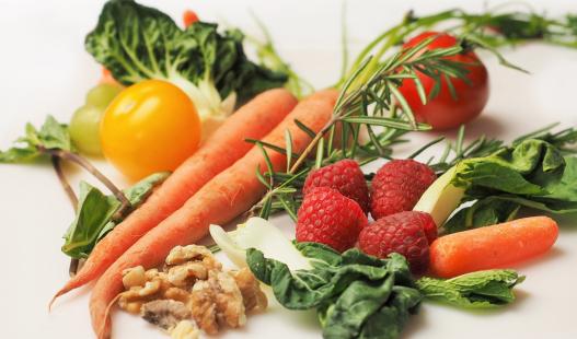 Assorted foods(raspberries, carrots, tomatoes, walnuts, various greens) across a tabletop