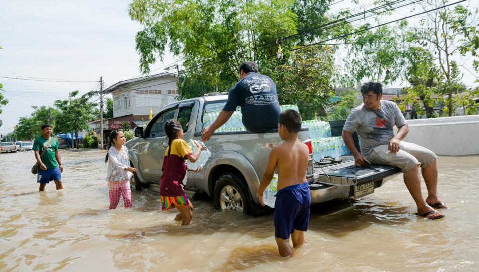 A group of people wading through a flooded street to a pick-up truck to receive containers of water.