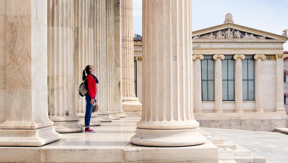 A young teenage girl looks up at the ceiling beneath the columns of the Athenian Academy in Athens, Greece.