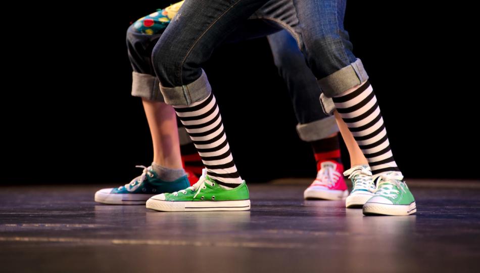 A close-up of the feet of three hip-hop dancers on stage, wearing colorful sneakers.