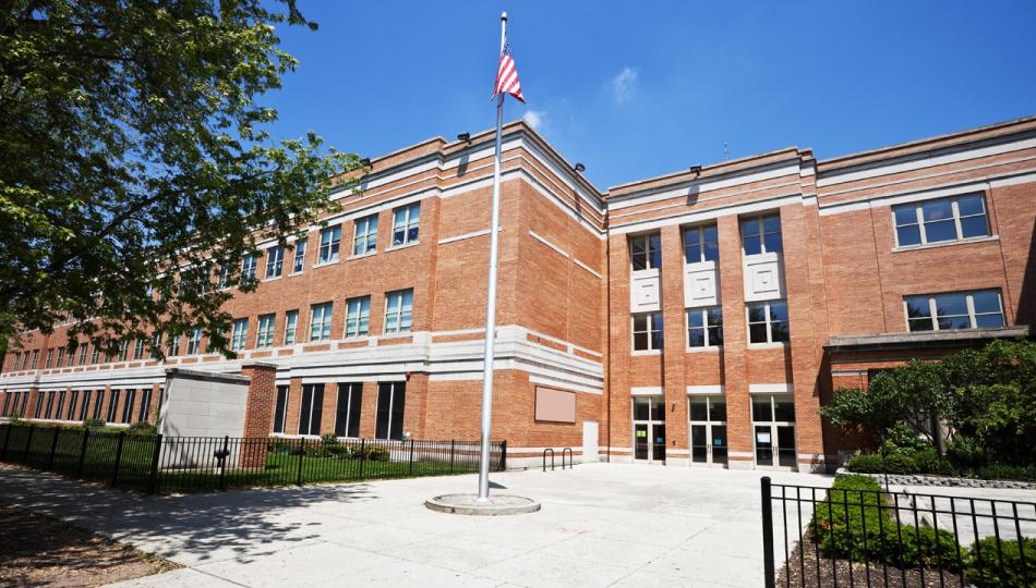 An exterior shot of a school with a flag pole in the courtyard on a sunny day.