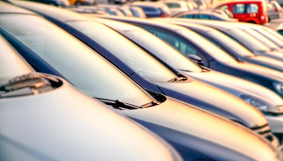 A row of parked cars on a public dealership at sunset.