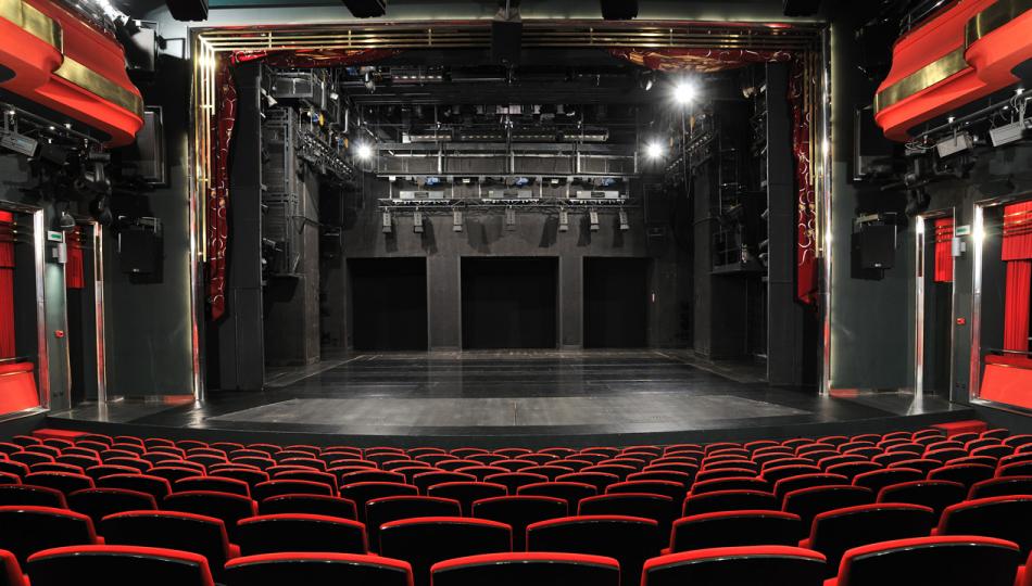 An empty, medium-sized theater with black and red seats as seen from the back row. 
