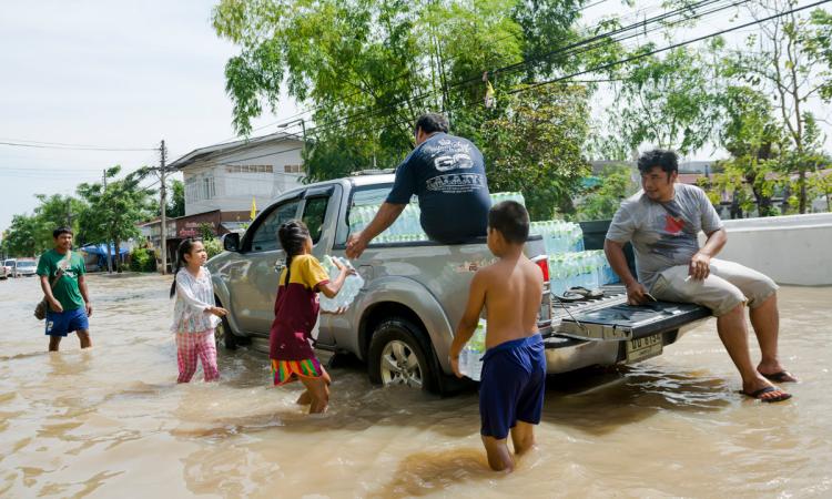 A group of people wading through a flooded street to a pick-up truck to receive containers of water.