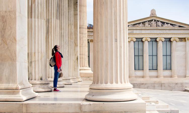 A young teenage girl looks up at the ceiling beneath the columns of the Athenian Academy in Athens, Greece.