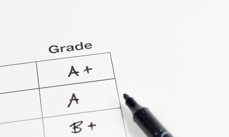 A freshly graded report card—featuring an A +, A and B + grades—with a felt-tip pen laying beside it.