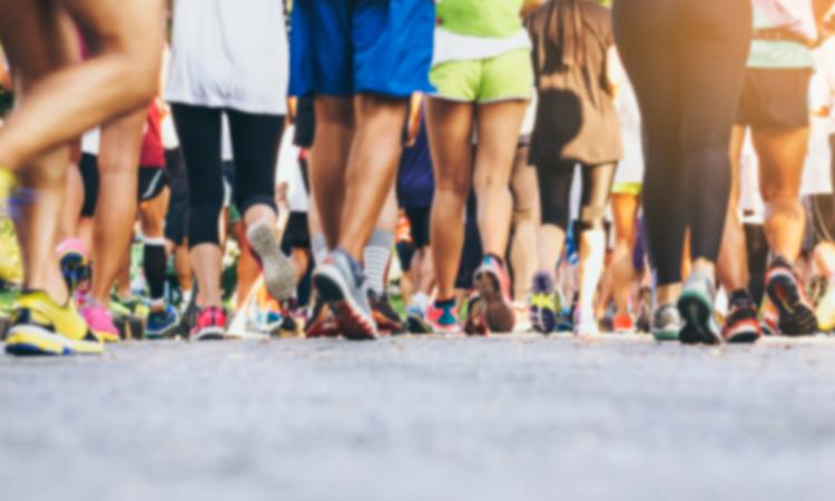 The legs of a couple dozen walkers participating in a race, with pavement featured prominently in the foreground.