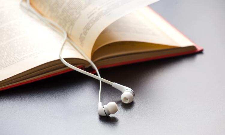 A book lies open on a desk, with a pair of white ear-buds acting as a bookmark.