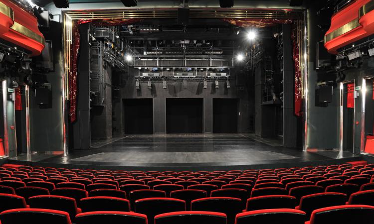 An empty, medium-sized theater with black and red seats as seen from the back row.