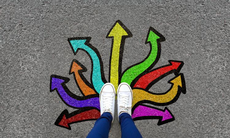 Birds eye view of a pair of shoes on cement, with multicolored arrows pointing from the shoes in different directions.