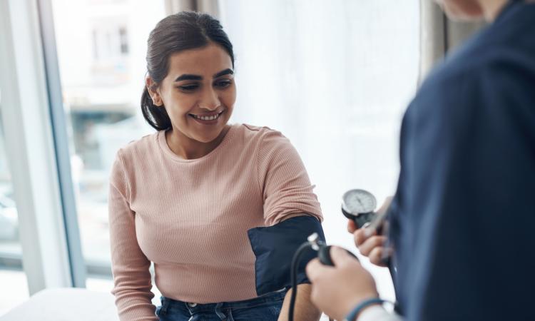 Woman in pink shirt getting blood pressure checked by a medical professional.