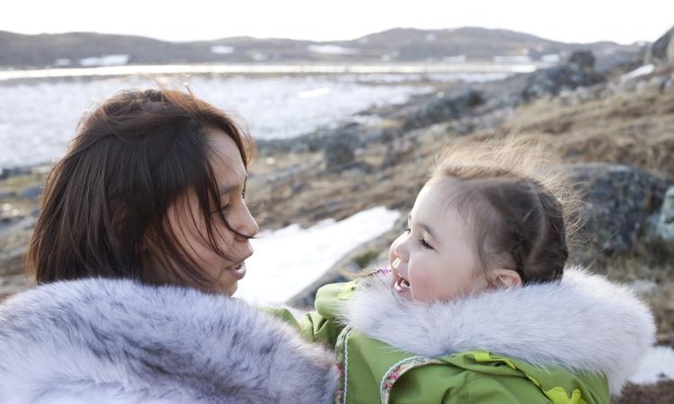 An Inuit mother and her daughter on the tundra of Baffin Island in late spring. They are interacting with each other. Background is rock, ice and distant mountains.