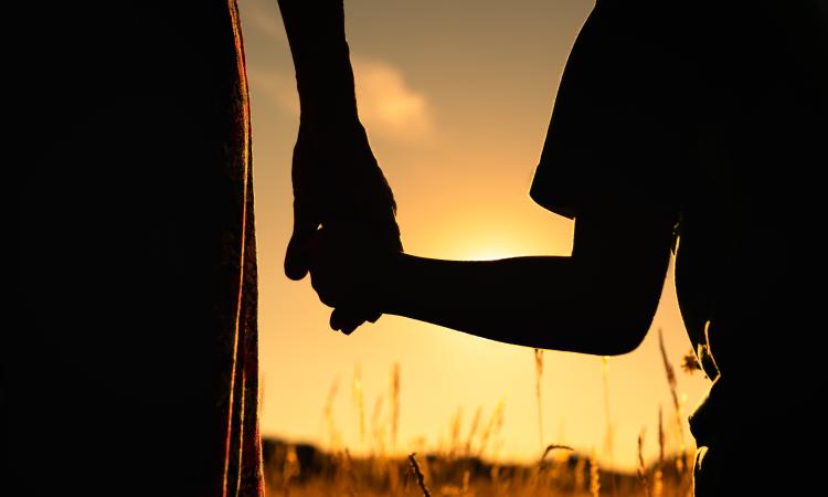 Silhouette of mother and child holding hands facing the sunset.