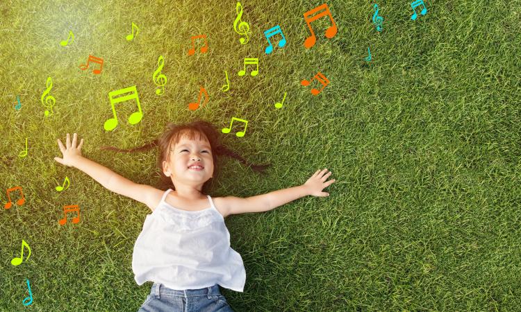 Little girl laying in the grass surrounded by music notes