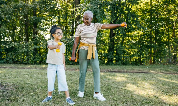 A young child and older woman exercising together with dumbbells in a park