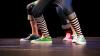 A close-up of the feet of three hip-hop dancers on stage, wearing colorful sneakers.