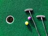 birds eye view of two miniature golf clubs, two balls, and a hole on a mini golf course